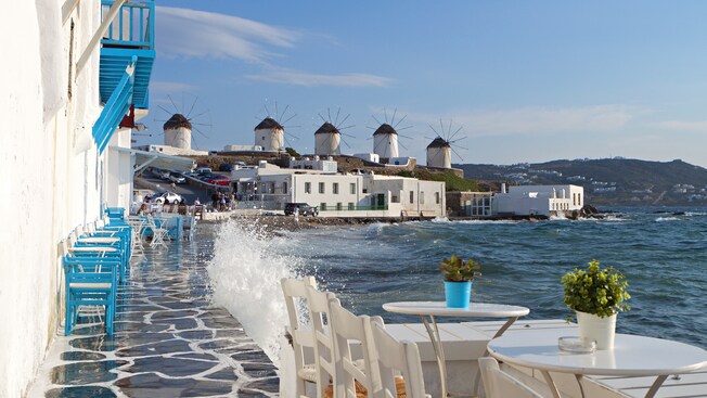 A series of windmills located on a hill near a beach with sidewalk cafes