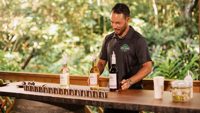 A bartender handles 3 bottles of rum at a bar lined with shot glasses A bartender handles 3 bottles of rum at a bar lined with shot glasses