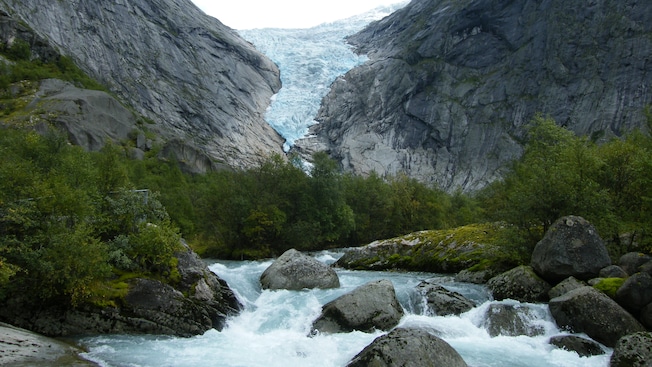 A rocky stream flowing through the mountains with the Briksdal Glacier in the background A rocky stream flowing through the mountains with the Briksdal Glacier in the background