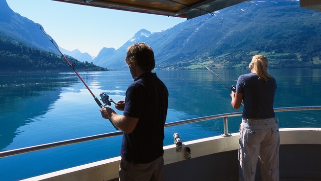 A man and woman fish from a Fjord aboard a boat