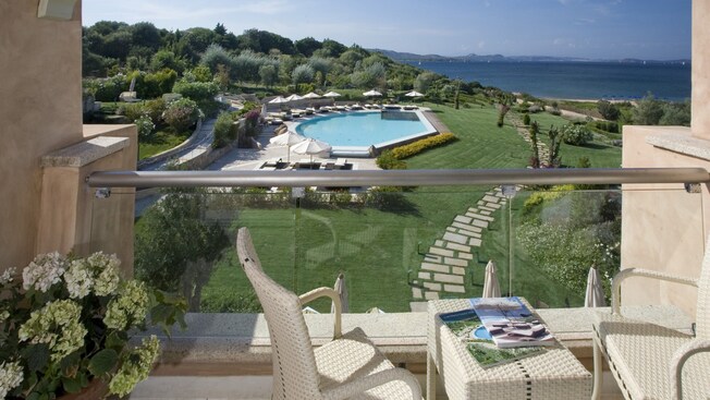 Un balcón con un área para sentarse que cuenta con vista a un área de piscina cerca de un bosque y al mar