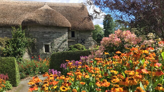 Un jardín al lado de una histórica casa de piedra con un tejado de paja