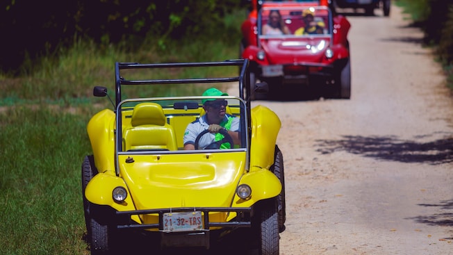 Um homem dirige um buggy de praia sem teto à frente de outros buggies Um homem dirige um buggy de praia sem teto à frente de outros buggies