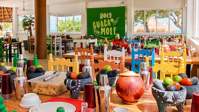 El alegre interior de un restaurante, con un letrero colgante que dice ‘Holy Guacamole’ y grandes ventanales que dan a la playa