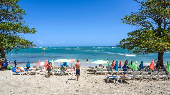 People sunbathing, lounging under umbrellas and participating in watersports at a tropical beach