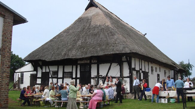 Guests dining outdoors near a historical building with a thatched roof