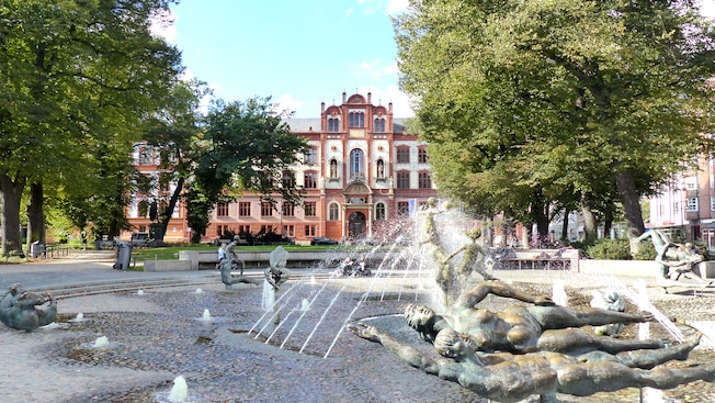 Mature trees and a large fountains with bronze statues in front of a monumental building Mature trees and a large fountains with bronze statues in front of a monumental building
