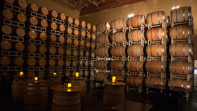 Candelitas encendidas en seis mesas en una sala revestida desde el piso hasta el techo con barriles de vino de madera Candelitas encendidas en seis mesas en una sala revestida desde el piso hasta el techo con barriles de vino de madera