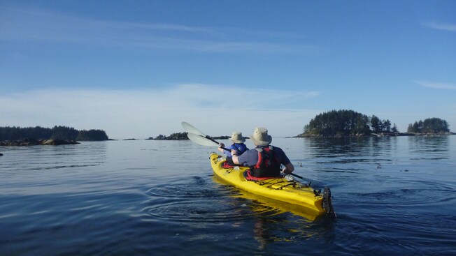 2 people in a 2 seat kayak paddling on a lake surrounded by verdant land masses