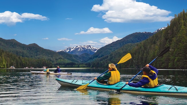 4 kayakers paddling through waters surrounded by forest and snowcapped mountains 4 kayakers paddling through waters surrounded by forest and snowcapped mountains
