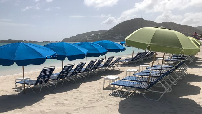 Outdoor recliners and umbrellas line the sand on a Caribbean beach, facing the water Outdoor recliners and umbrellas line the sand on a Caribbean beach, facing the water