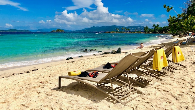 3 lounge chairs on the shore of a sandy beach 3 lounge chairs on the shore of a sandy beach