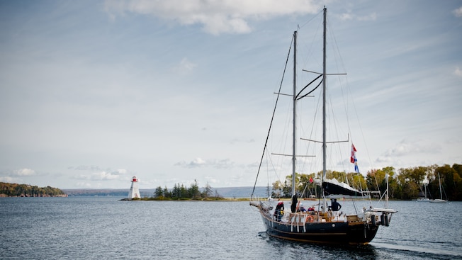 A schooner carries passengers toward a lighthouse in a narrow channel A schooner carries passengers toward a lighthouse in a narrow channel