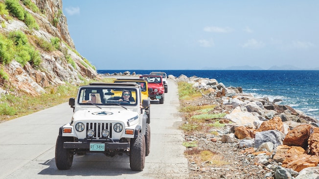 Pessoas dirigem quatro Jeep Wranglers em uma estrada costeira nas montanhas próximo ao oceano Pessoas dirigem quatro Jeep Wranglers em uma estrada costeira nas montanhas próximo ao oceano