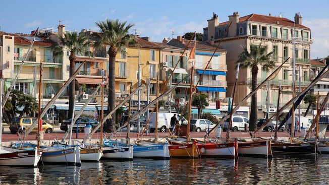 A promenade next to a harbor filled with boats and lined by sidewalk cafes and beach residences