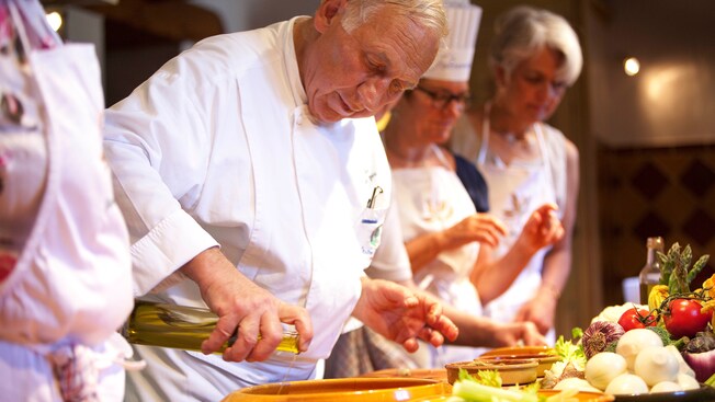 A chef drizzling oil into a wooden salad bowl during a cooking class