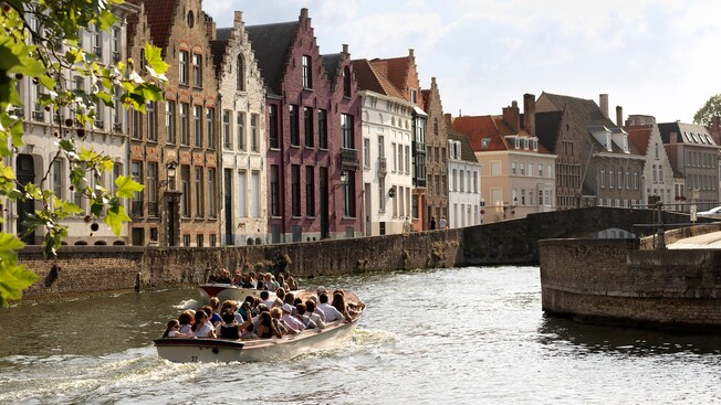 2 boats filled with passengers traveling through a waterway lined with historical buildings