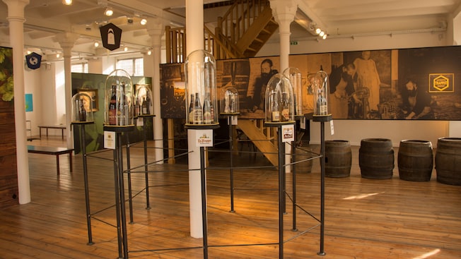 Beer bottles on stands enclosed by glass stand on display in front of beer barrels, historic images and a staircase Beer bottles on stands enclosed by glass stand on display in front of beer barrels, historic images and a staircase