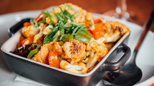 Coliflor Kung Pao en un plato estilo cazuela junto a una cuchara