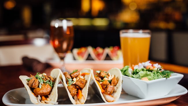 A glass of draft beer and a platter featuring 3 Short Rib Tacos and a salad