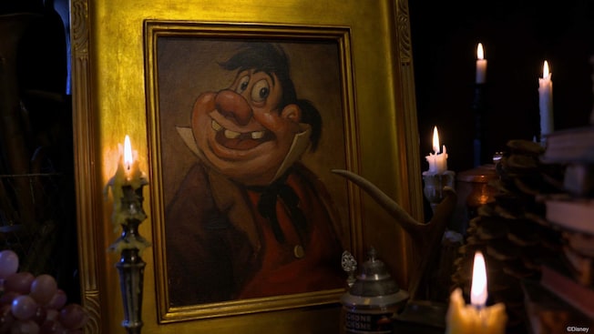 Candles and books surround a gold framed image of Beauty and the Beast's LeFou character