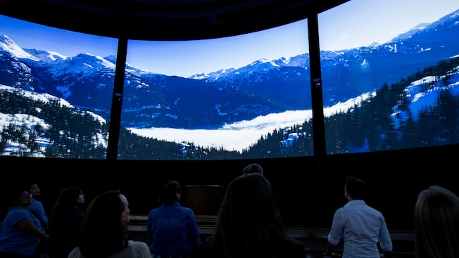 Guests stand in 360 theatre watching a beautiful video of snow and mountains in Canada