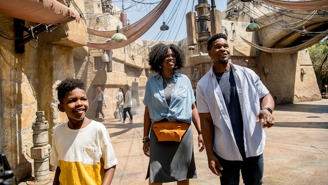 Parents and their son walk through an alley with light fixtures and drapes hanging from the walls
