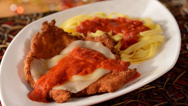 A breaded chicken cutlet covered with parmesan cheese and a tomato sauce with a side of linguini and tomato sauce, all on one plate