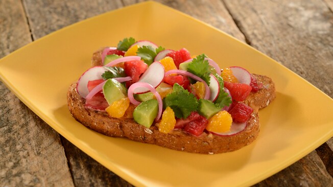 A piece of toast topped with avocado, tomatoes, oranges, onions and mayonnaise