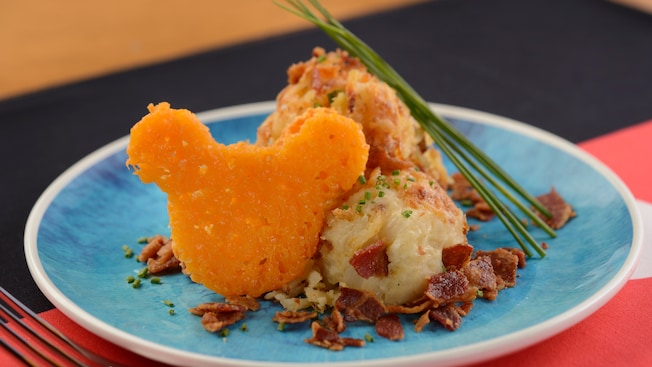 Un plato con orejas de Mickey hechas de queso, junto a papas batidas adornadas con trozos de tocineta y puerros