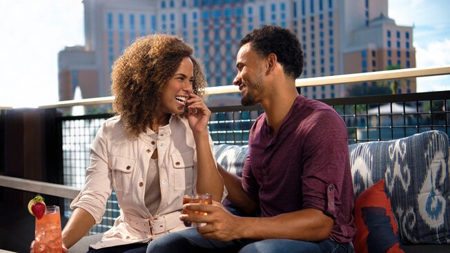 Una pareja en una mesa en el patio, riendo y sosteniendo bebidas