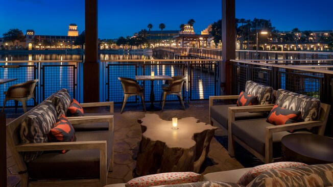 Una mesa de madera con una vela iluminada, rodeada de sillas frente a ventanas con vista a la laguna
