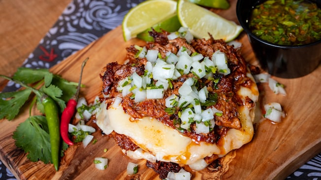 A beef mixture with cheese garnished with onions, parsley, cilantro and peppers and served on a wooden platter