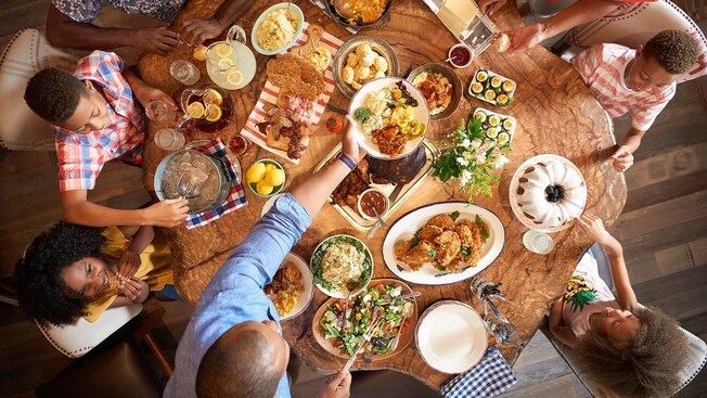 A family sits around a table with assorted shareable entrees, starters, beverages and dessert