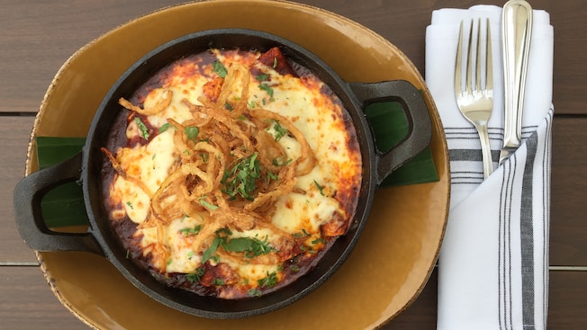 Enchiladas served in a cast iron dish and topped with melted cheese, crispy onion and cilantro