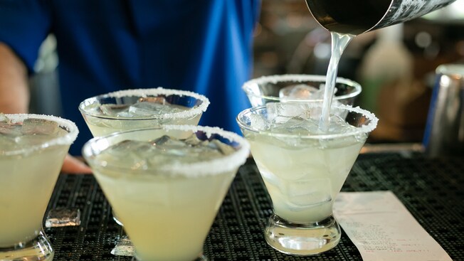 A bartender pouring a freshly made margarita cocktail into glasses with ice and salted rims
