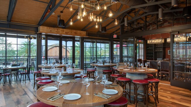 A large wine bar with an open ceiling and barrel themed tables
