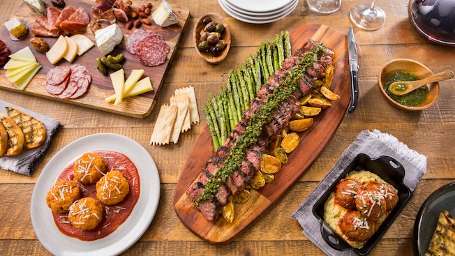 A large spread of charcuterie, meatballs, macaroni and cheese, and cuts of steak with asparagus