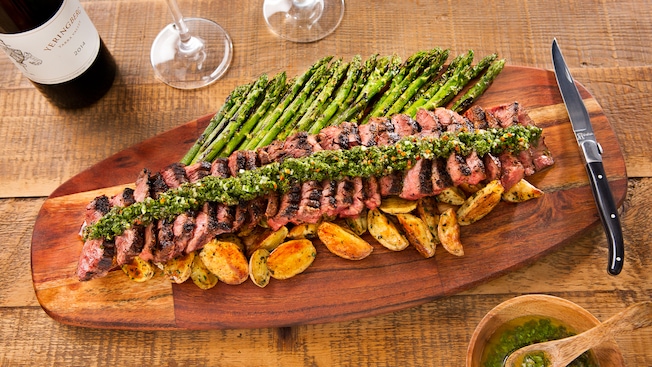 Skirt steak with roasted potatoes, chimichurri and asparagus served on a wooden platter