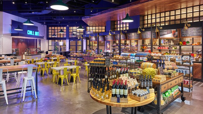 A quick service dining location with stations for ordering snack and beverages and tables with chairs for two or four people