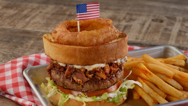Um anel de cebola sobre um hambúrguer ao lado de batata frita de acompanhamento	