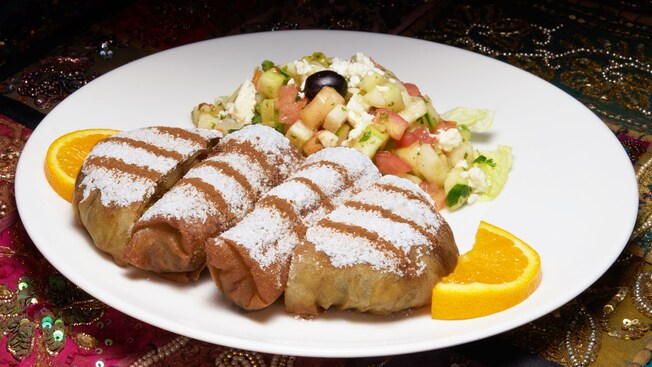 A large plate with powdered savory pastries and a salad, garnished with orange wedges