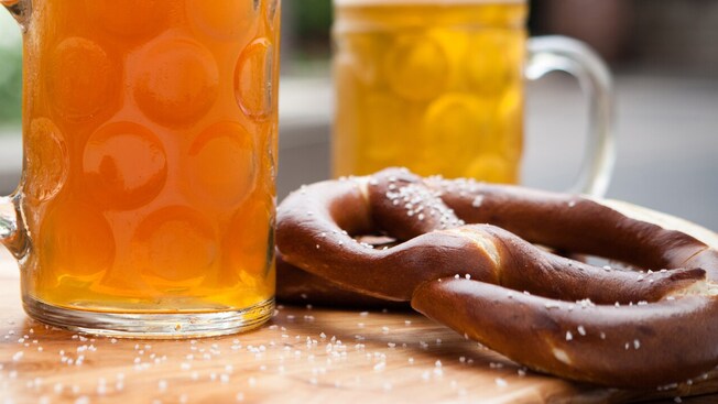 A salted soft pretzel next to 2 steins of beer