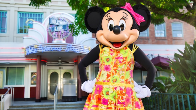 Minnie Mouse wearing a floral dress and a bow in front of Hollywood & Vine restaurant