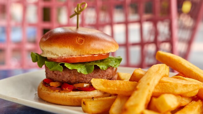 Una hamburguesa con lechuga, salsa, tomate y más en un panecillo, servida al plato con papas fritas