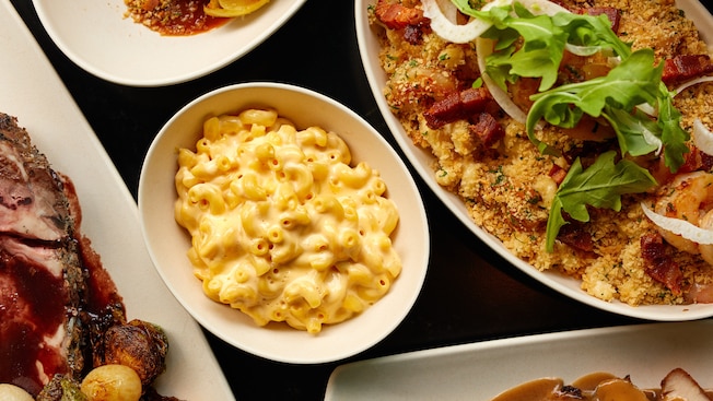 Mac and cheese in a center dish surrounded by plates of other dinners