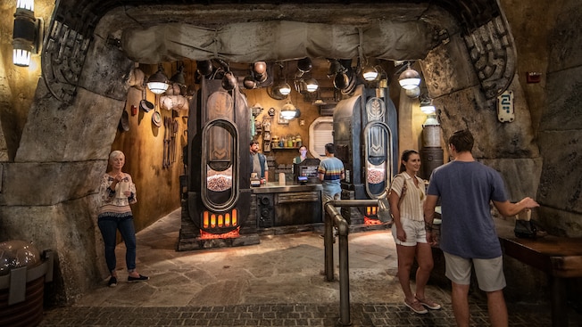 The stone archway leading into Kat Sakas, with 3 guests shopping in the store and 2 cast members behind the counter