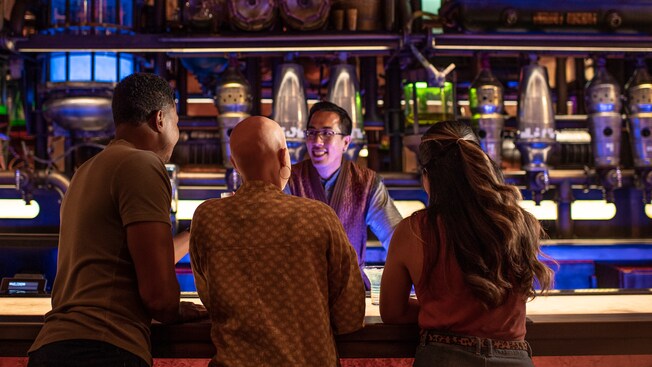 A bartender interacts with 3 customers standing at the bar