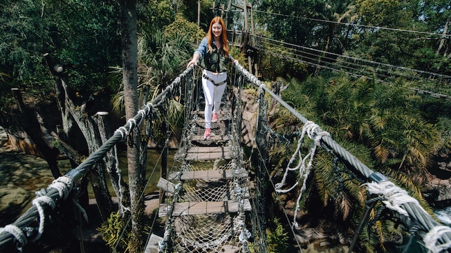 A woman with a harness smiles as she crosss a rope bridge