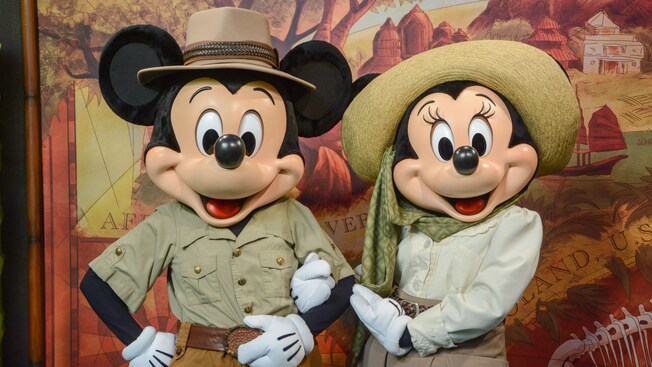 Mickey Mouse and Minnie Mouse pose together, arm in arm, in safari attire